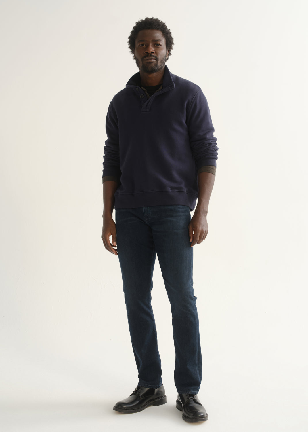 Person wearing a dark navy long sleeve shirt, dark indigo jeans, and black boots, front full body view on a light grey background.