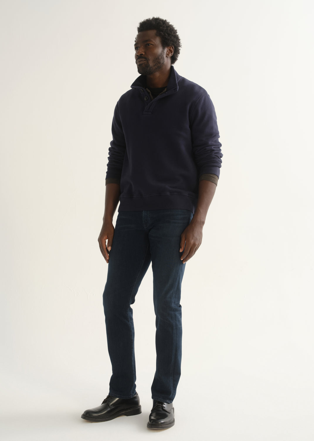 Person wearing a dark navy long sleeve shirt, dark indigo jeans, and black boots, angled front full body view on a light grey background.