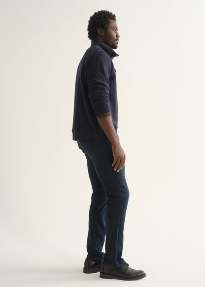 Person wearing a dark navy long sleeve shirt, dark indigo jeans, and black boots, side full body view on a light grey background.