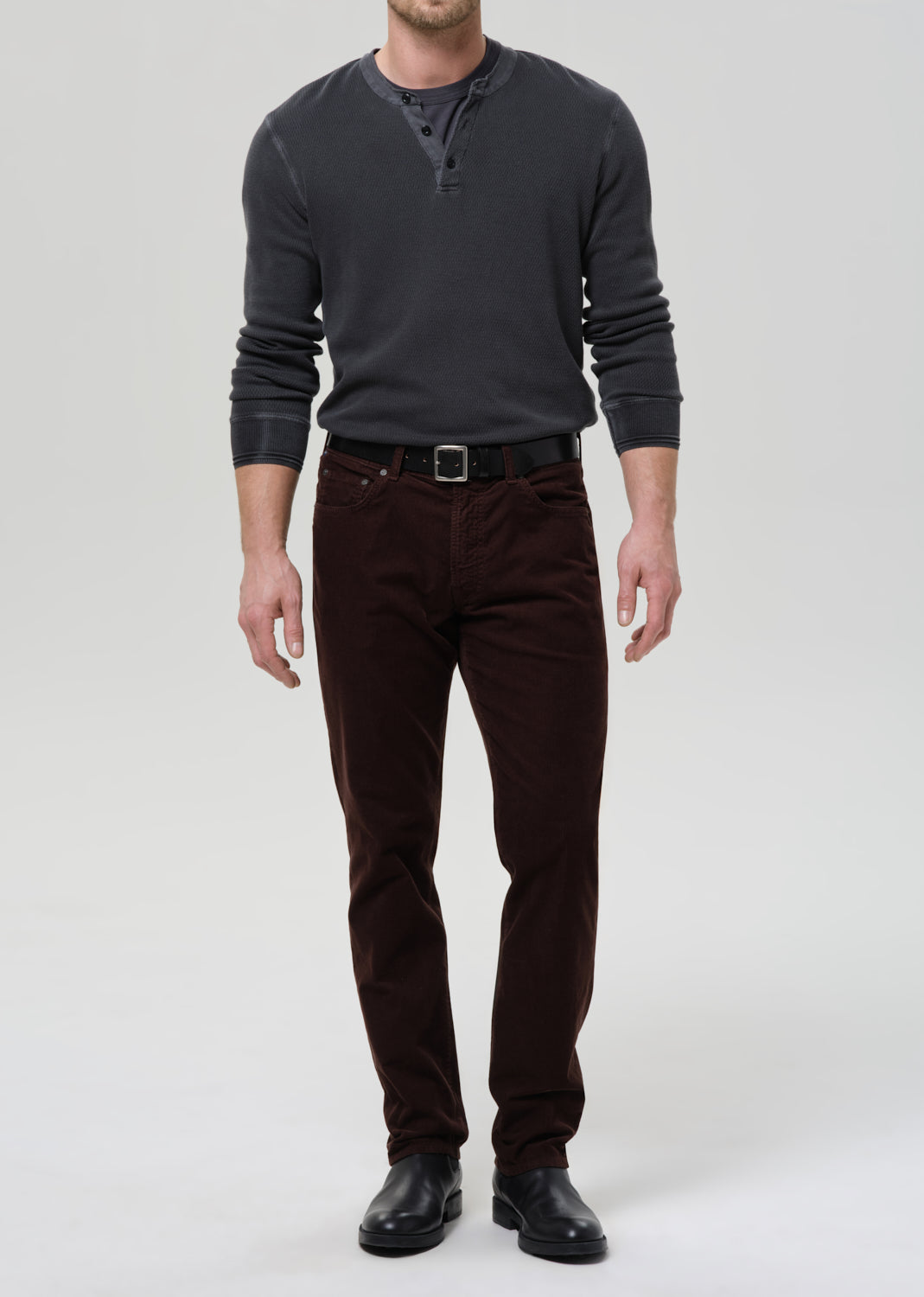 Man wearing a dark gray sweater and brown pants on a grey background