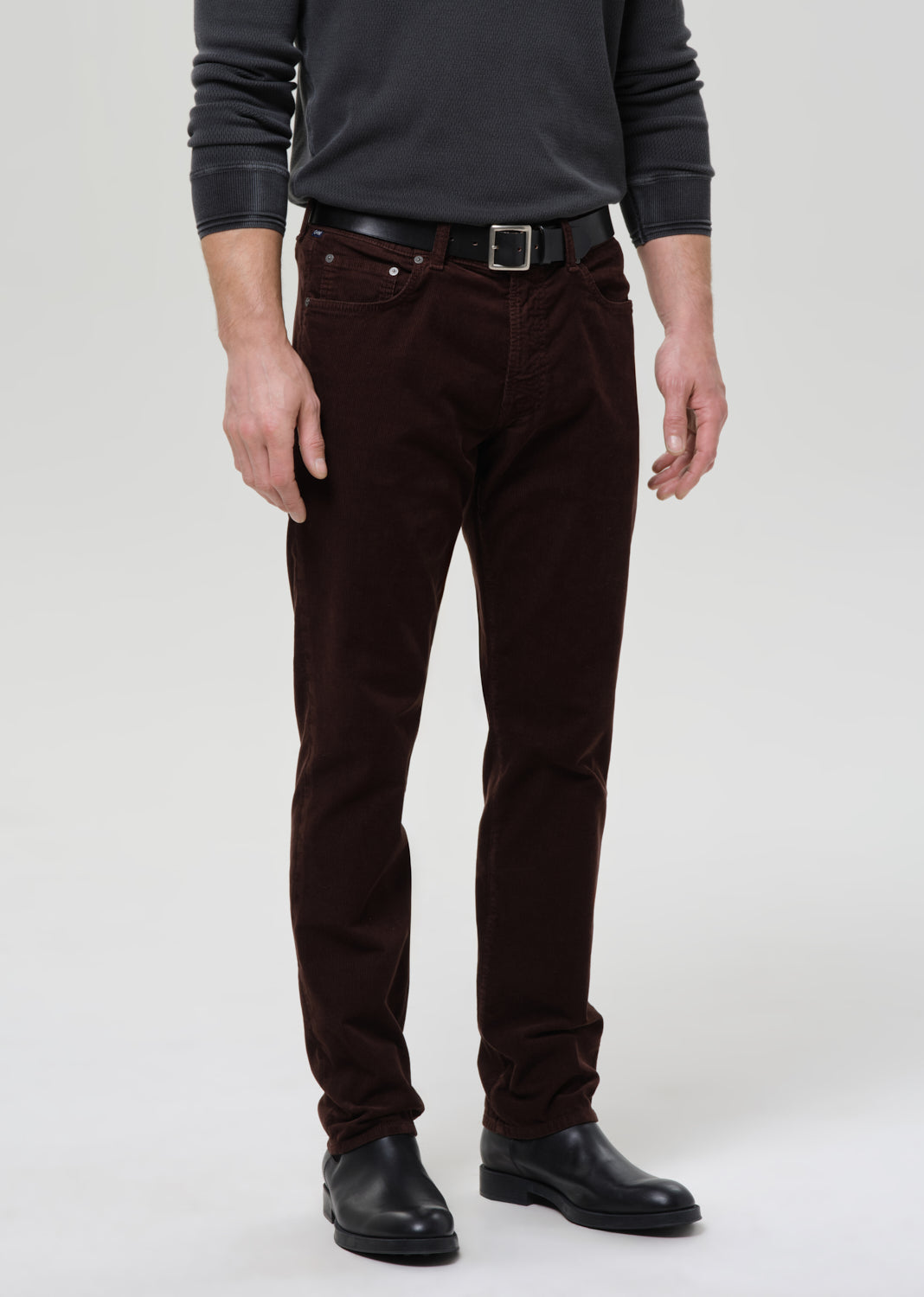 Person wearing brown pants and black shoes on a grey background