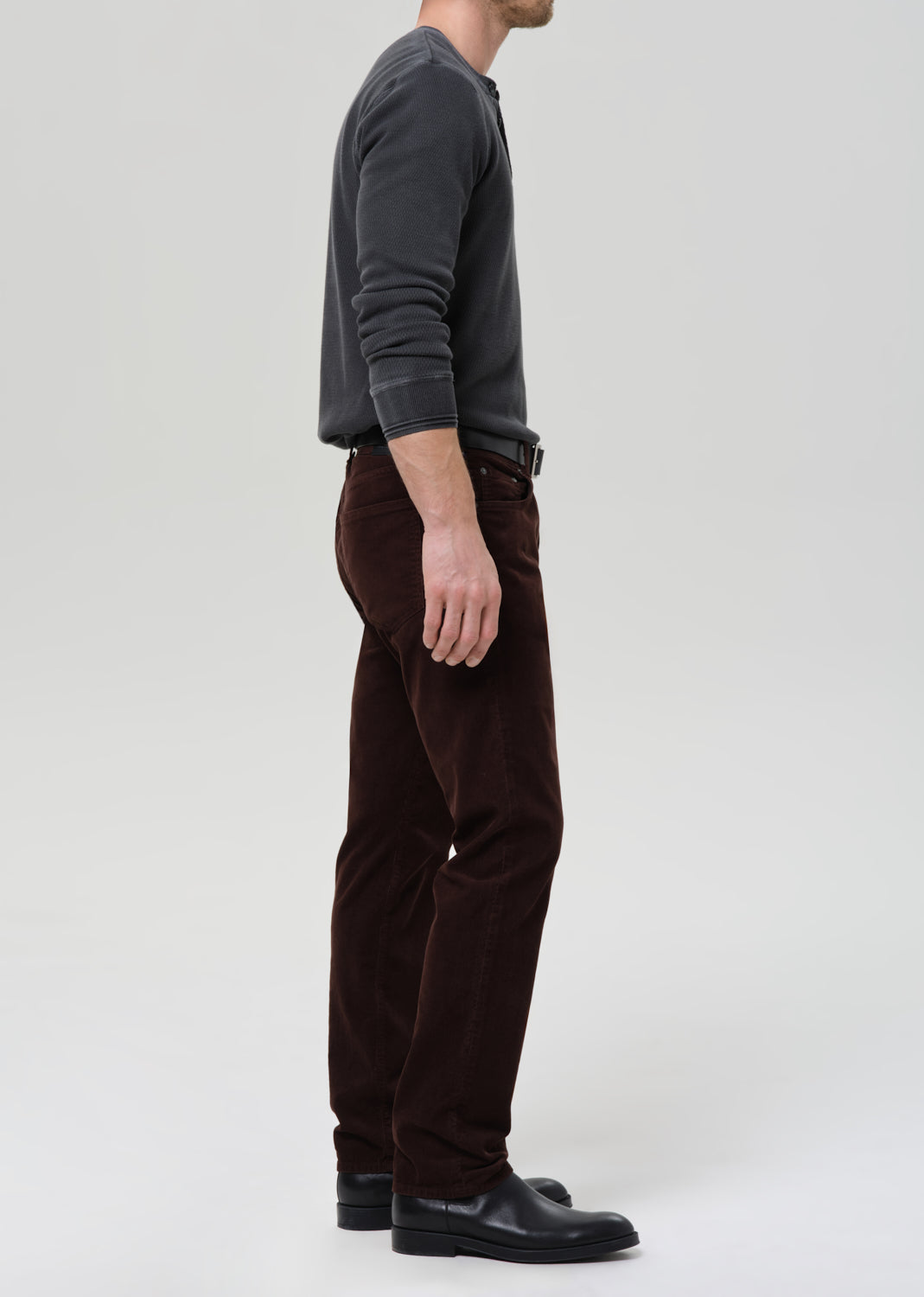 Person wearing a gray sweater and brown pants on a grey background