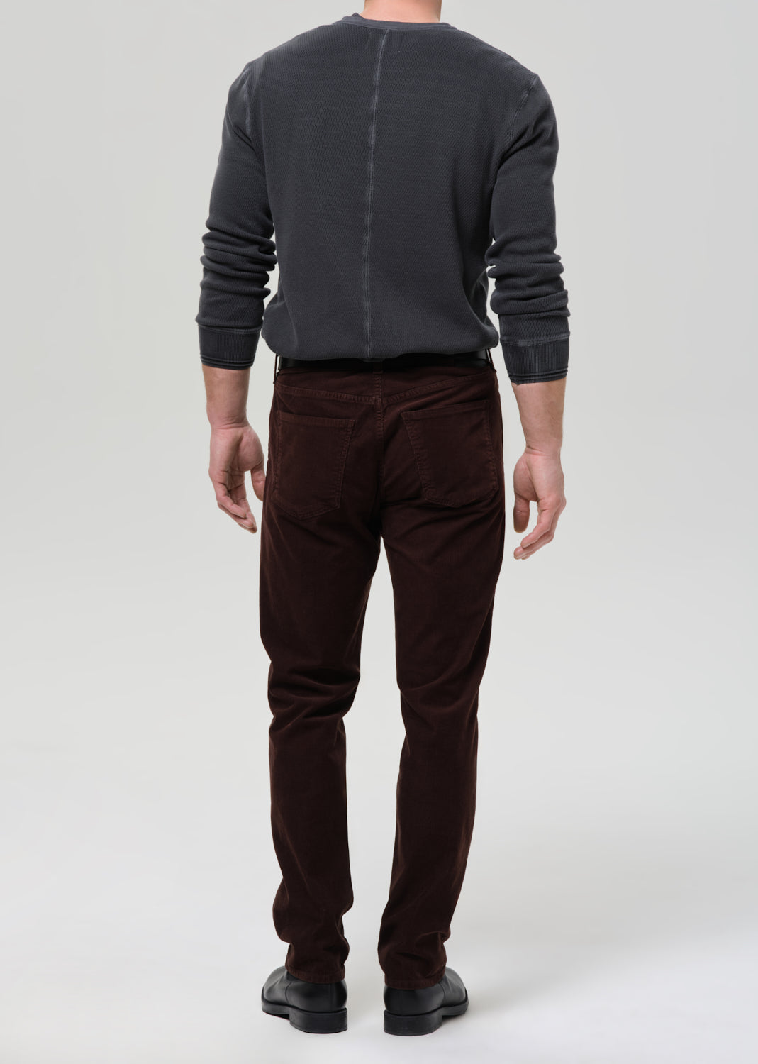 Person wearing a dark gray sweater and brown pants on a grey background