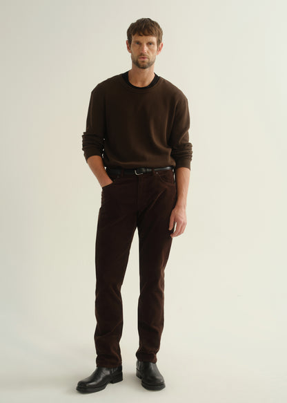Person wearing a dark brown crewneck sweater, dark brown pants, and black boots, front full body view on a light grey background.