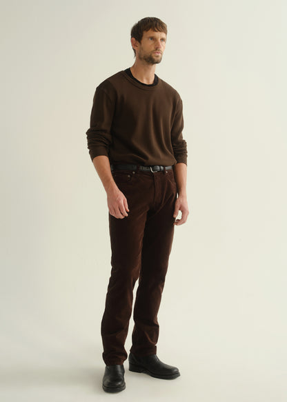 Person wearing a dark brown crewneck sweater, dark brown pants, and black boots, angled front full body view on a light grey background.