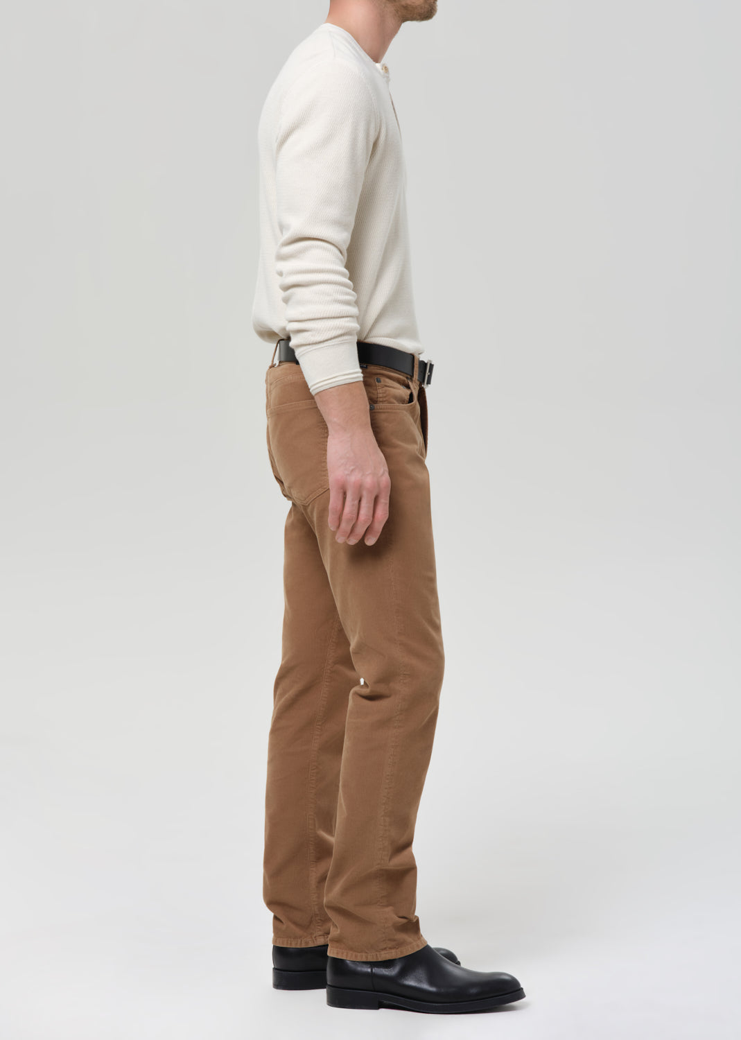 Person wearing a cream sweater and brown pants on a grey background