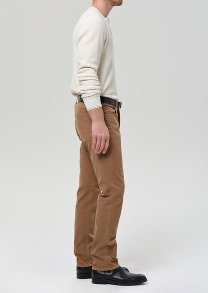 Person wearing a cream sweater and brown pants on a grey background
