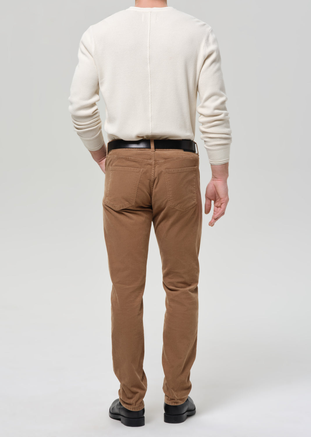 Person wearing a beige sweater and brown pants on a grey background
