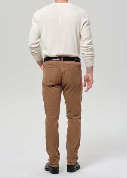 Person wearing a beige sweater and brown pants on a grey background