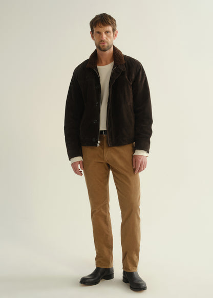 Person wearing a dark brown jacket, black shirt, tan corduroy pants, and black boots, front full body view on a light grey background.