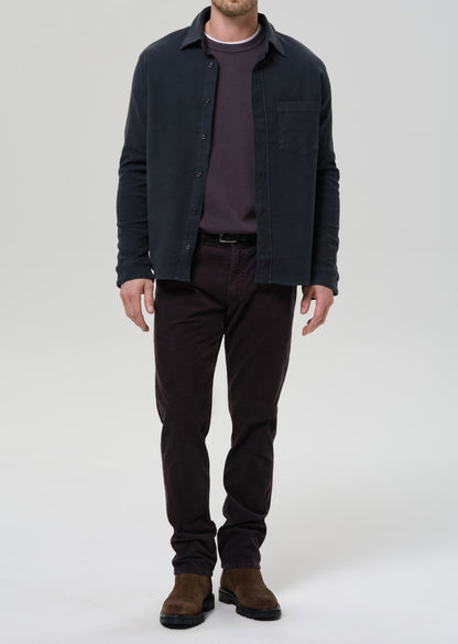 Man wearing a dark jacket, shirt, pants, and shoes on a grey background