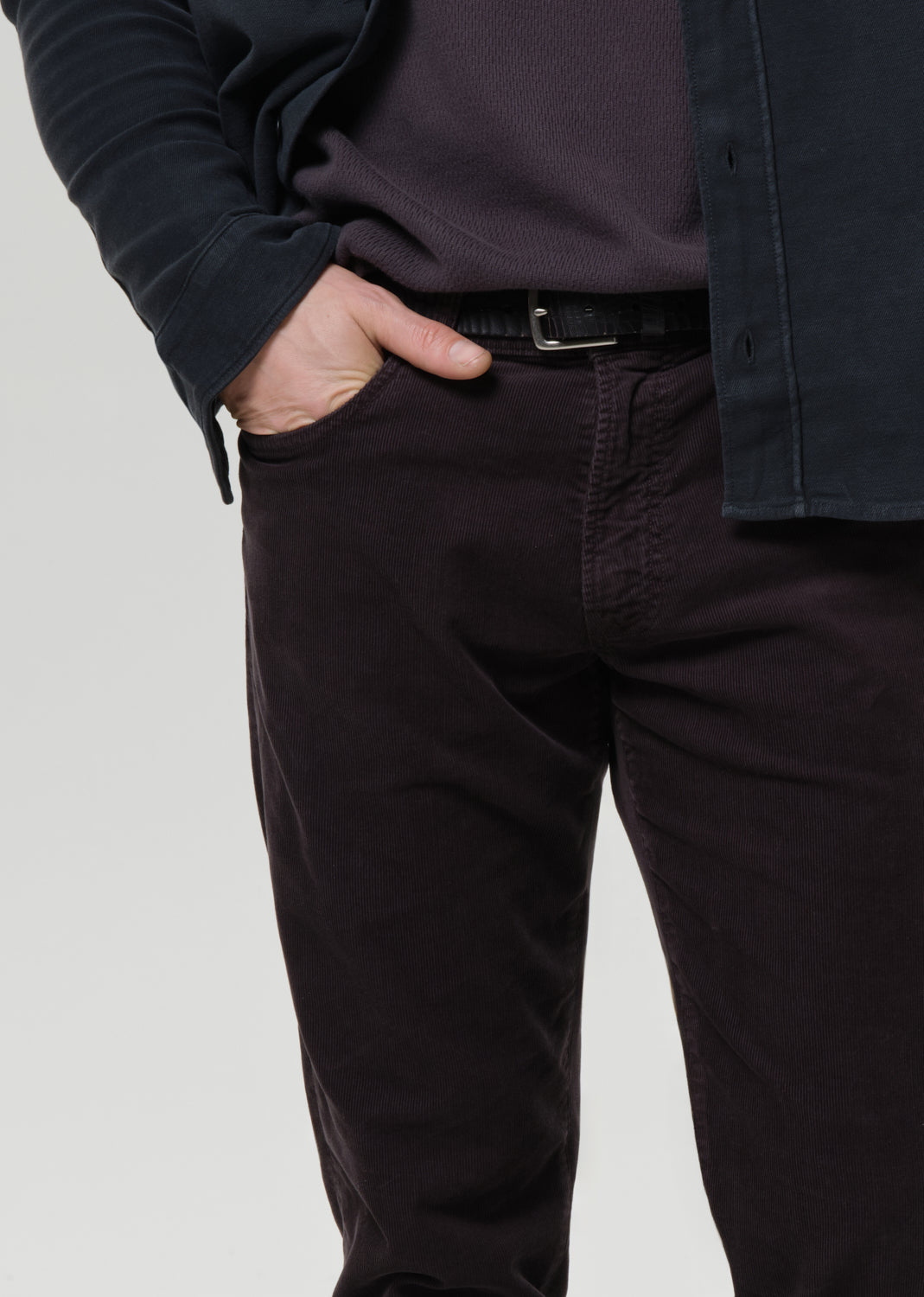 Person wearing dark pants and a jacket on a grey background