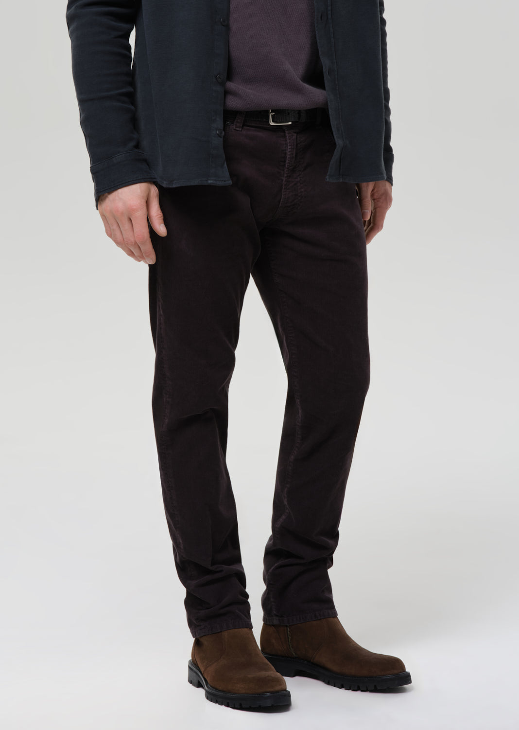 Person wearing dark pants and a jacket on a grey background