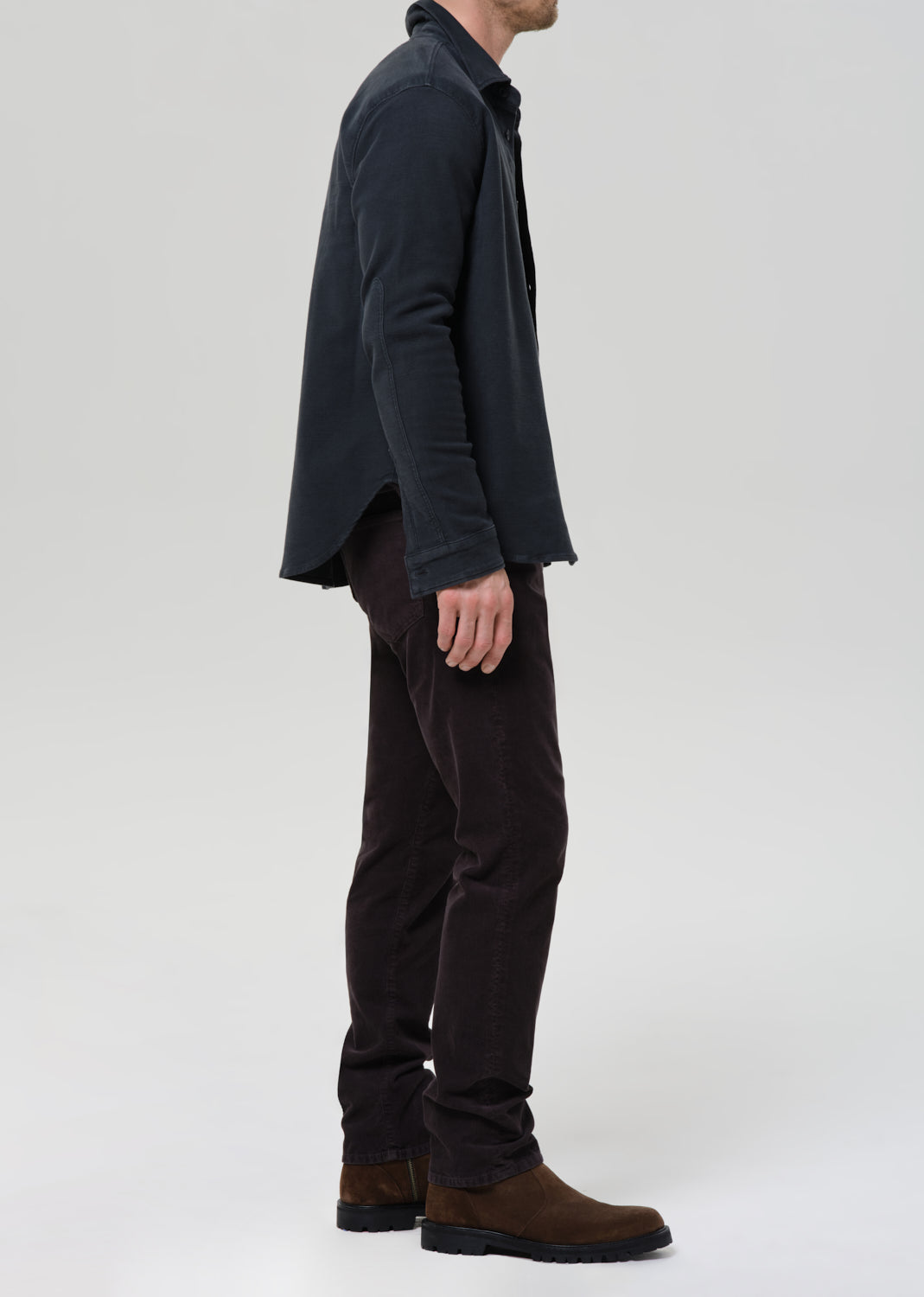 Person wearing a dark jacket and pants with brown shoes on a grey background