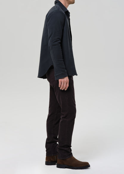 Person wearing a dark jacket and pants with brown shoes on a grey background