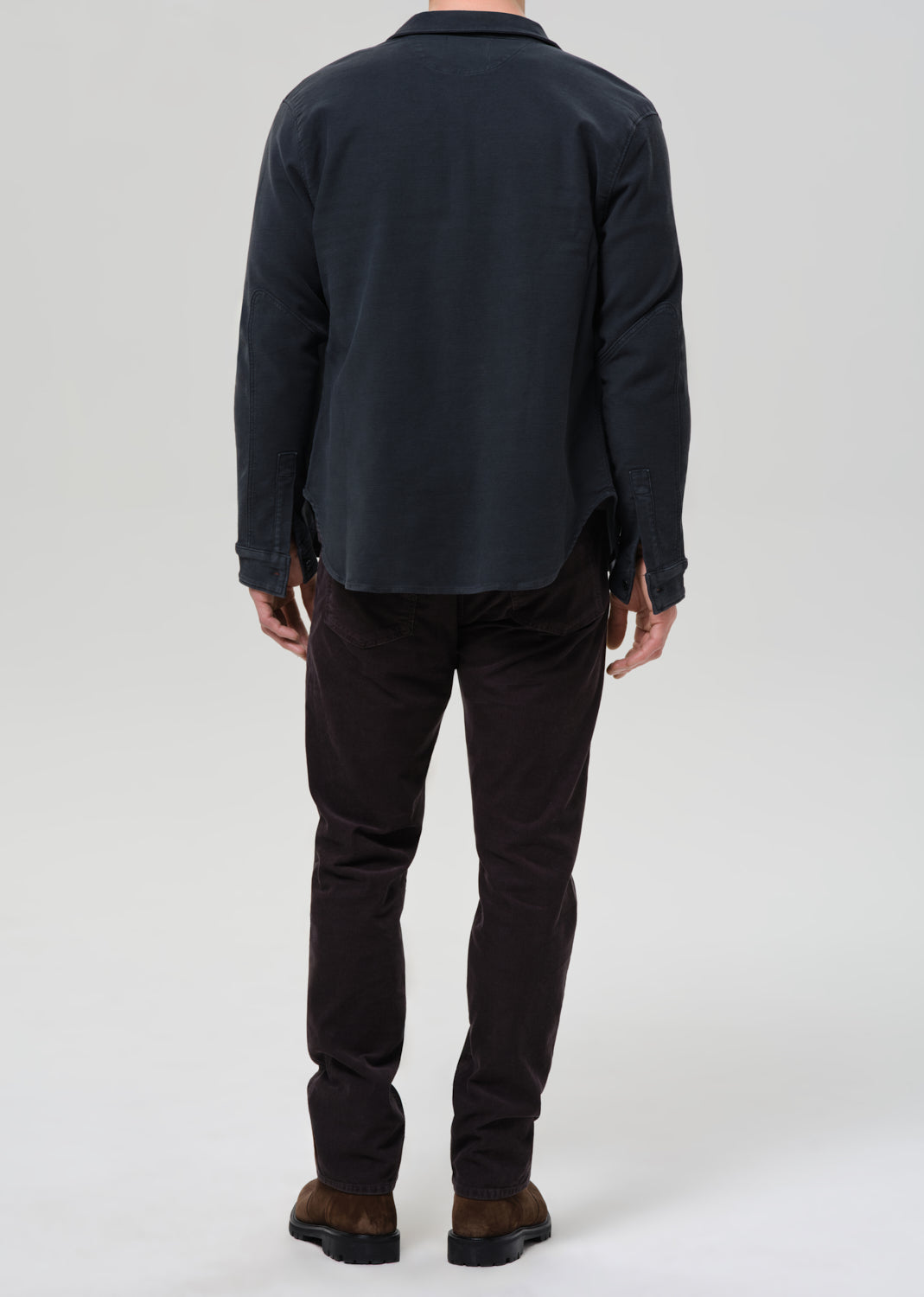Person wearing a dark jacket and black pants on a grey background