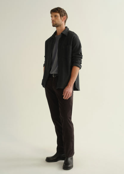 Person wearing a dark navy button-front shirt, washed black jeans, and black boots, angled front full body view on a light grey background.
