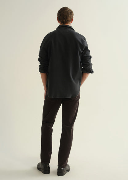 Person wearing a dark navy button-front shirt, washed black jeans, and black boots, back full body view on a light grey background.