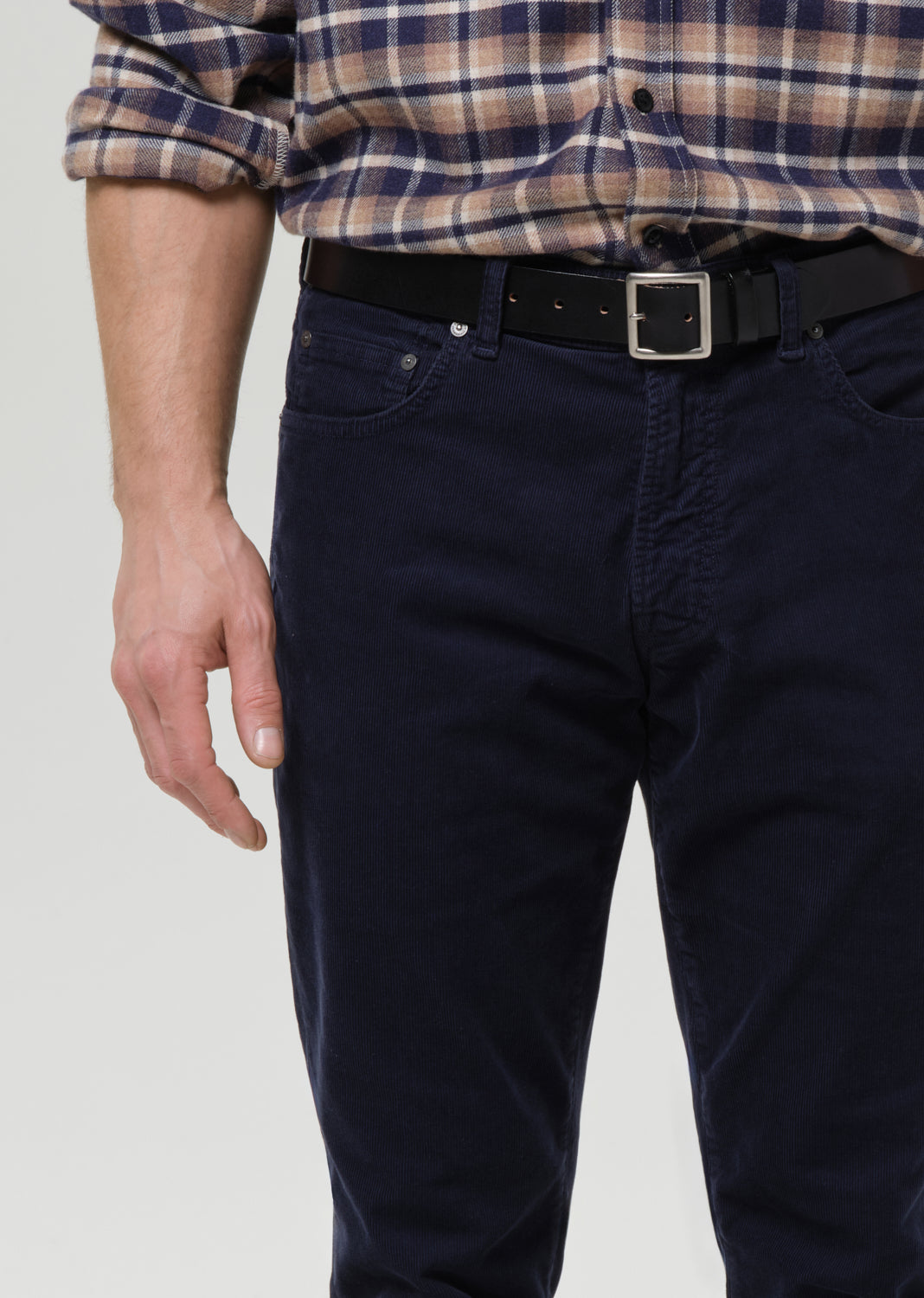 Person wearing a plaid shirt and dark jeans on a grey background