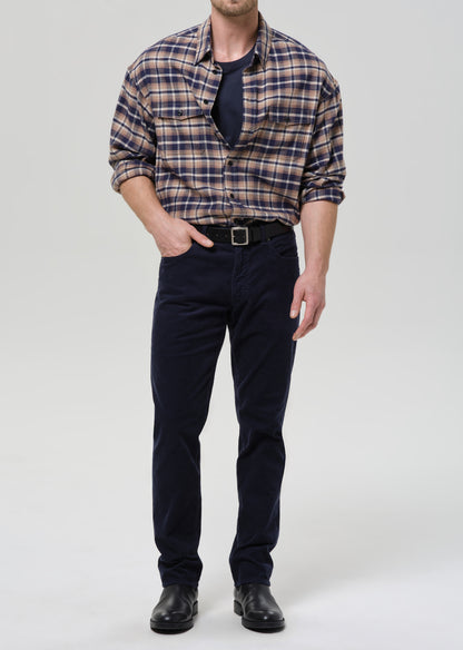 Man wearing a plaid shirt, navy pants, and black shoes on a grey background