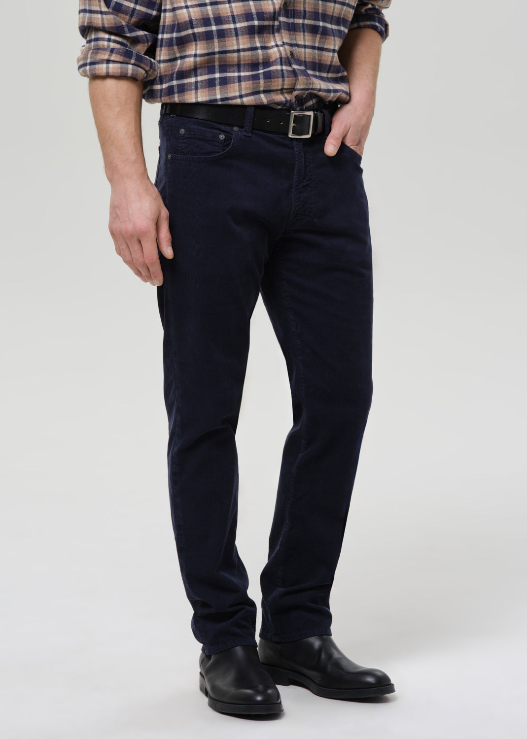 Person wearing navy blue jeans and a plaid shirt on a grey background