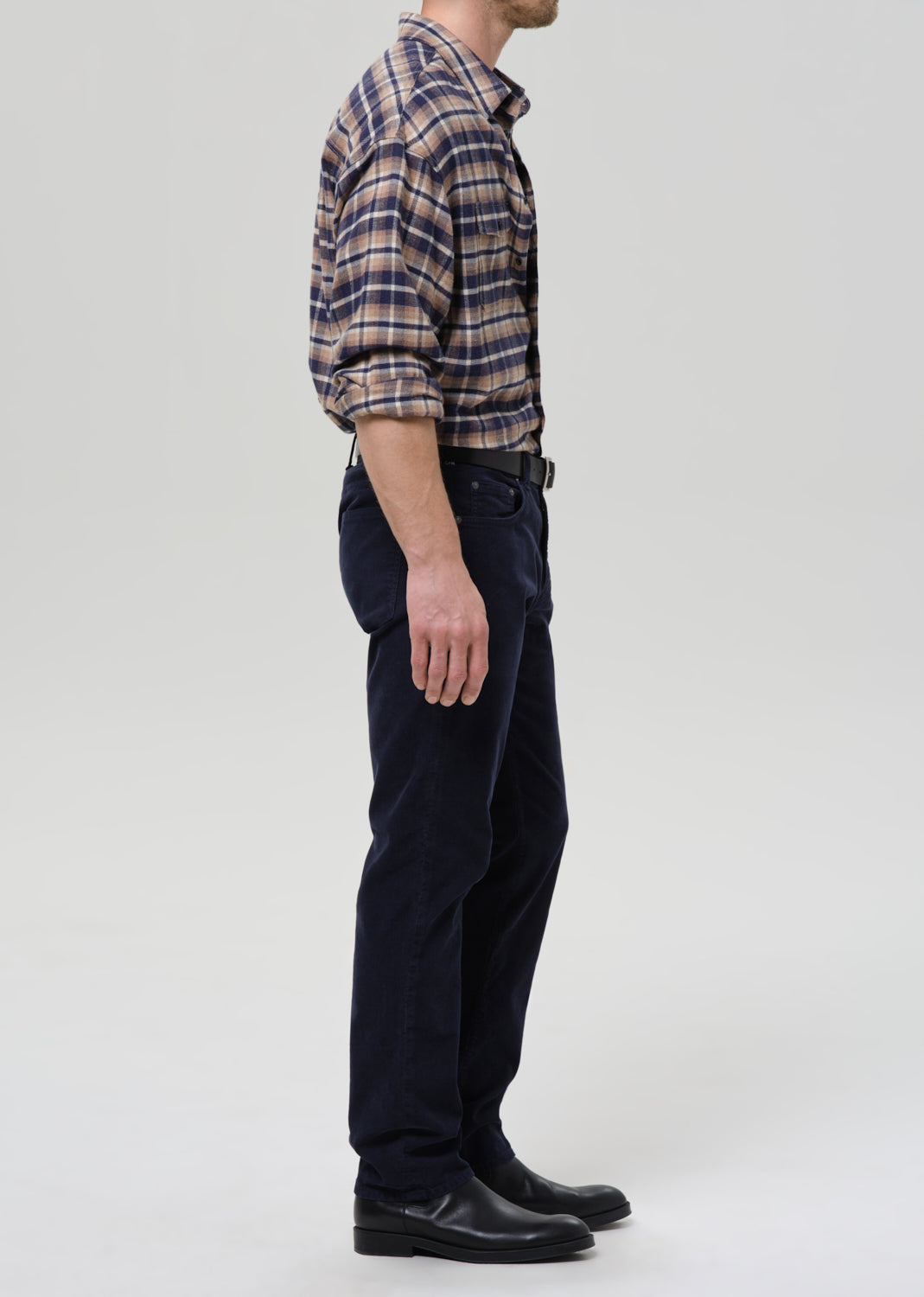 Person wearing a plaid shirt and dark pants on a grey background