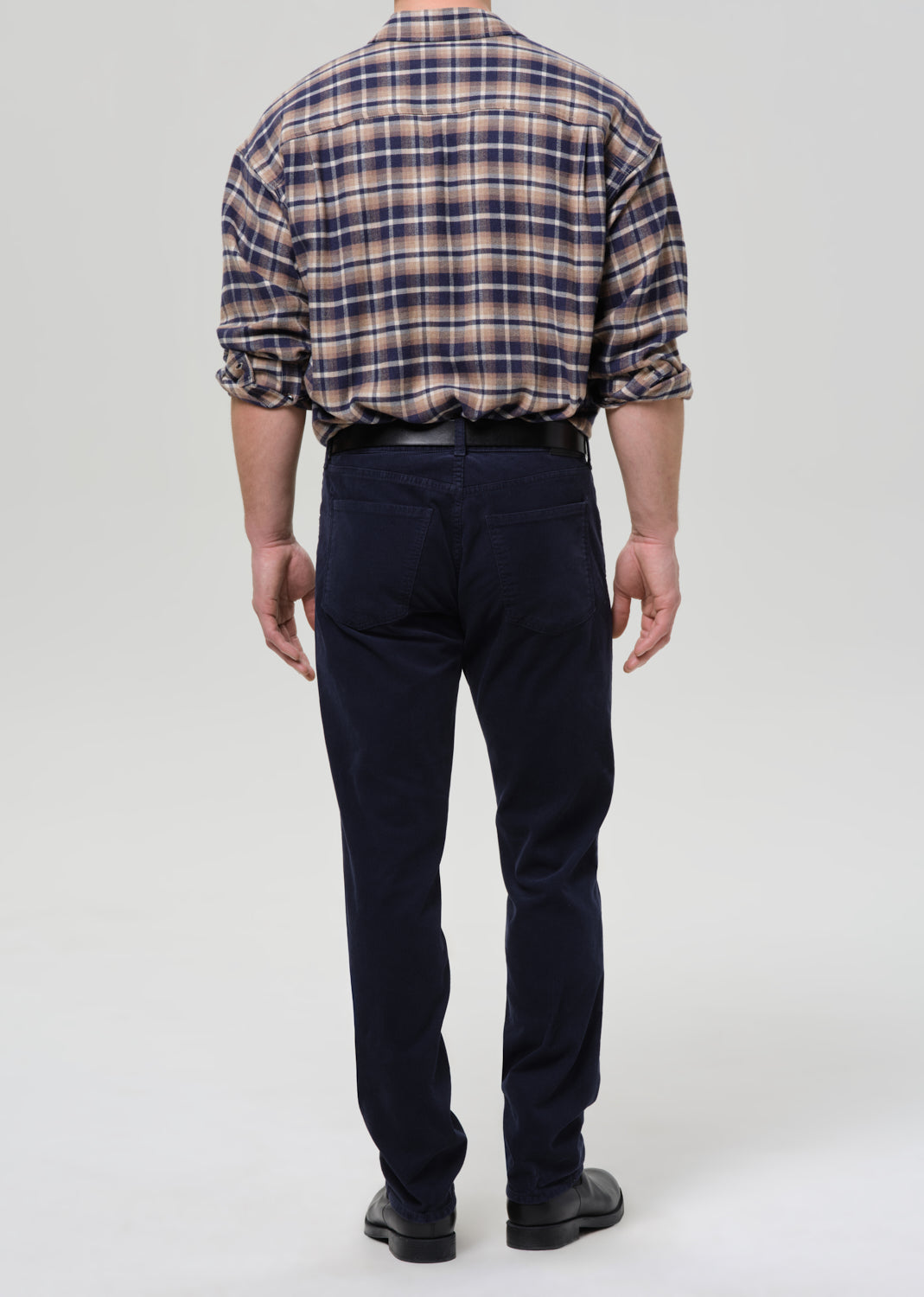 Person wearing a plaid shirt and dark pants on a grey background