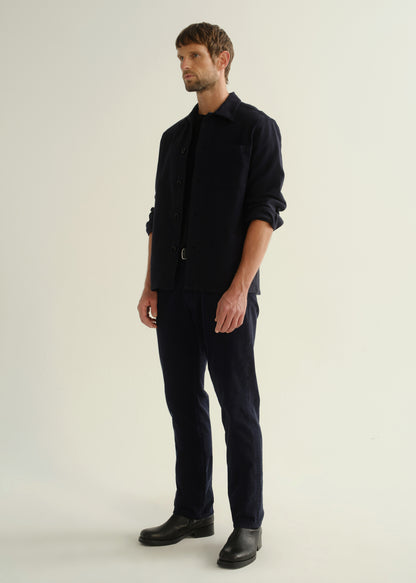 Person wearing a dark navy button-front shirt, dark indigo jeans, and black boots, angled front full body view on a light grey background.