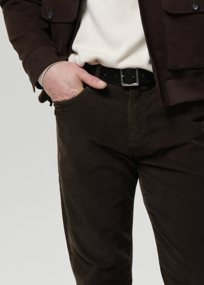Person wearing a brown jacket and dark green pants on a grey background