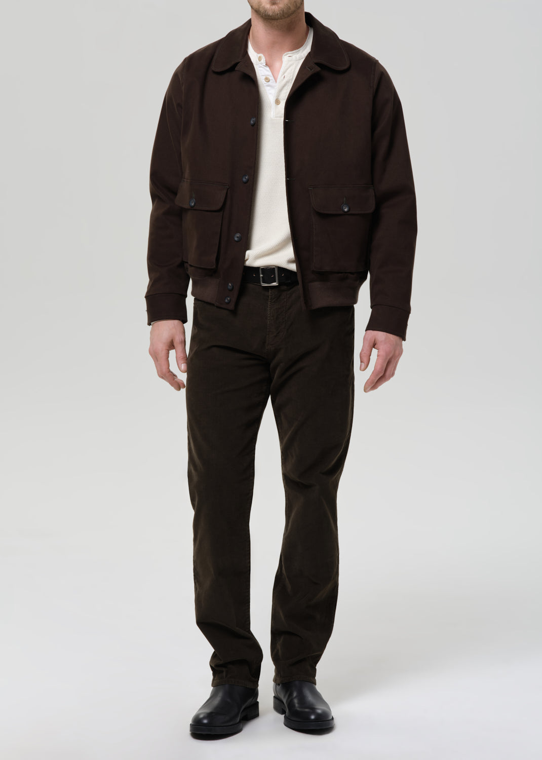 Man wearing a brown jacket and dark green pants on a grey background