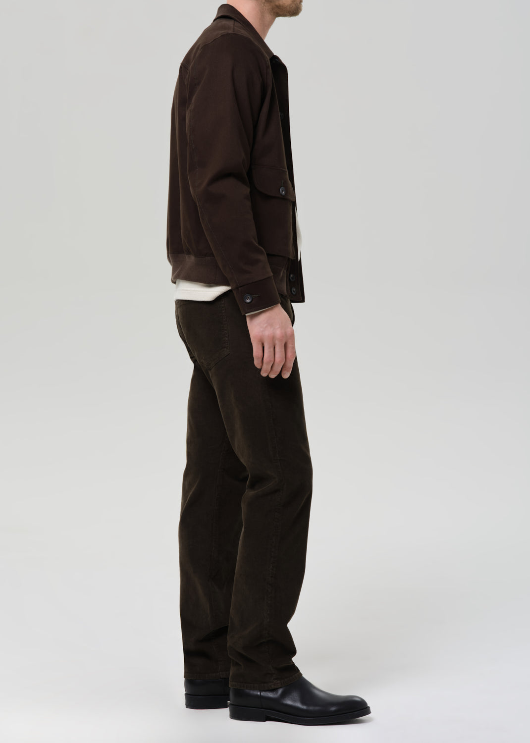 Person wearing a brown jacket and dark green pants on a grey background
