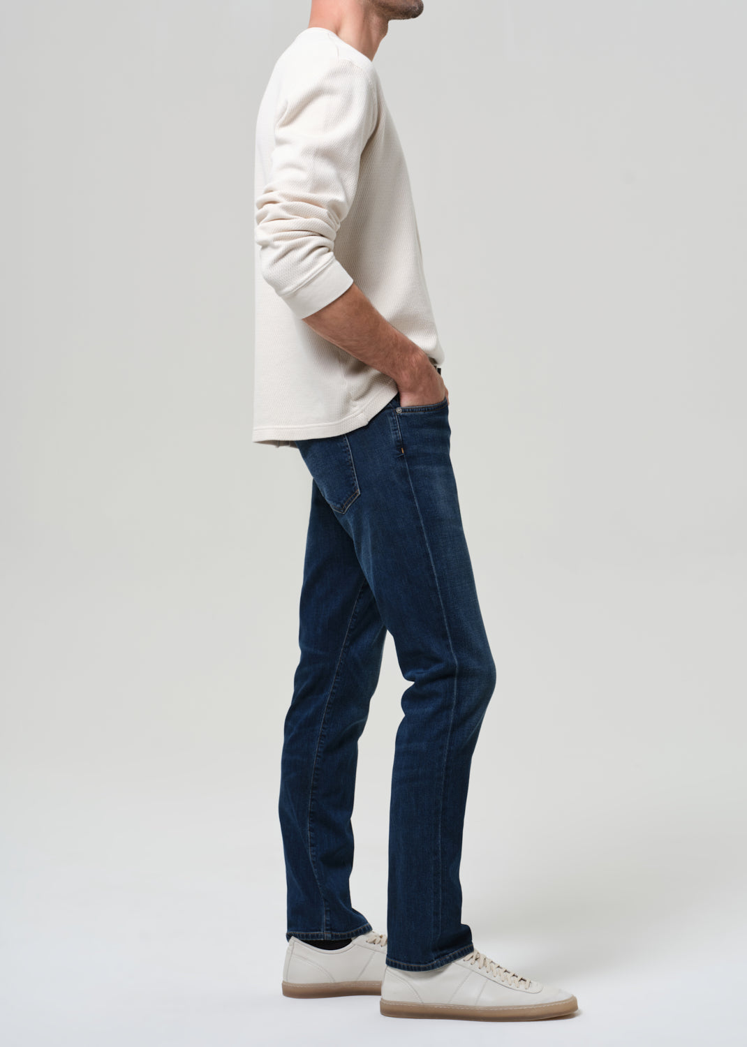 Person wearing a white sweater and blue jeans on a plain background