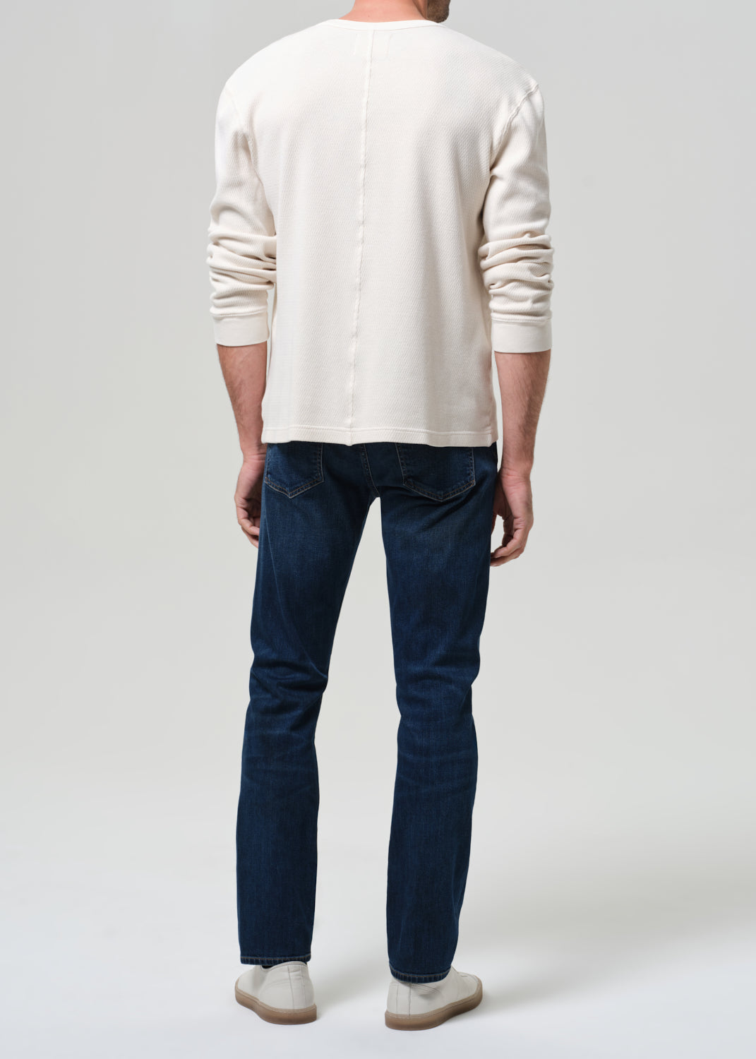 Person wearing a white sweater and blue jeans on a plain background