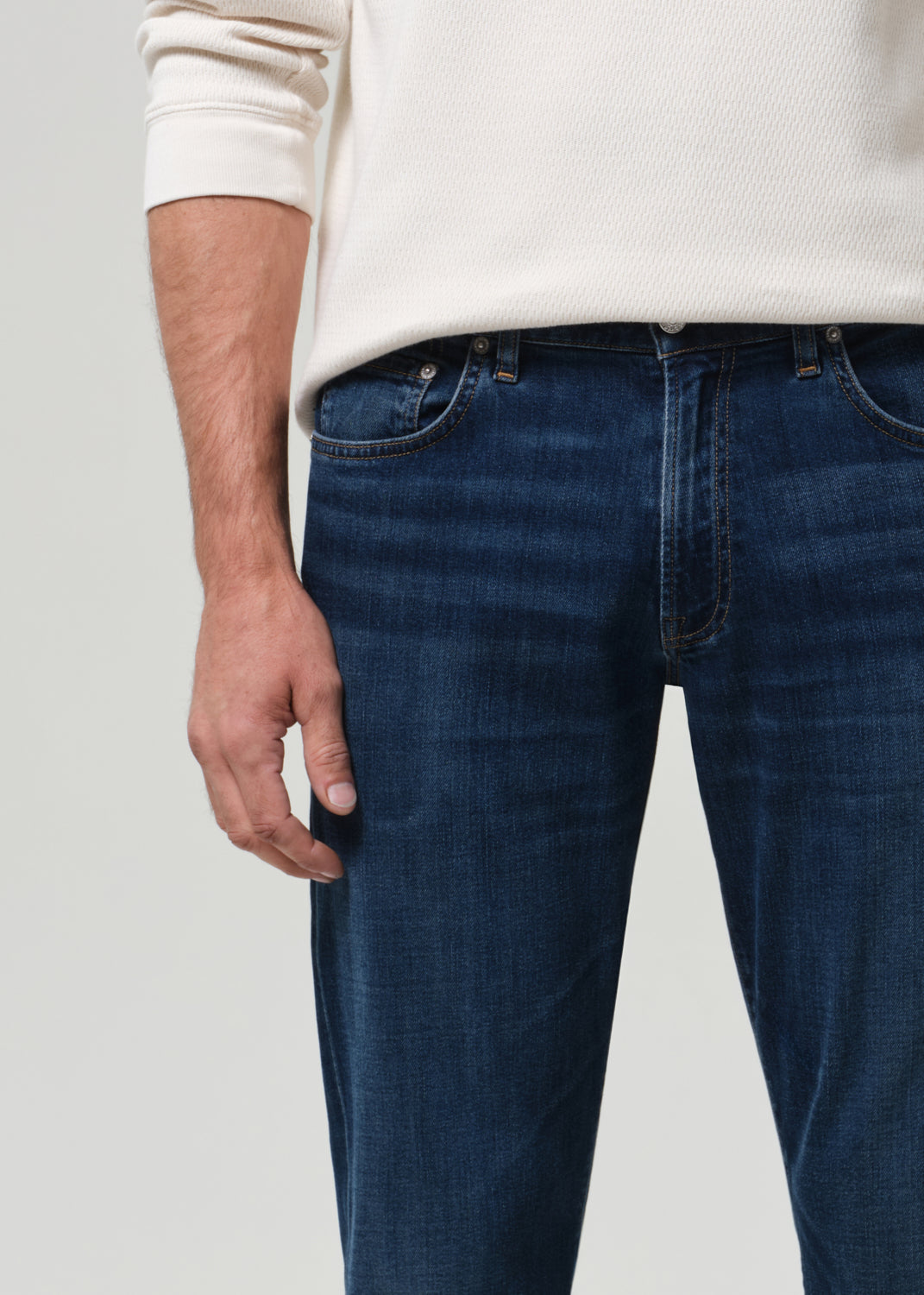 Person wearing blue jeans and a white sweater on a plain background