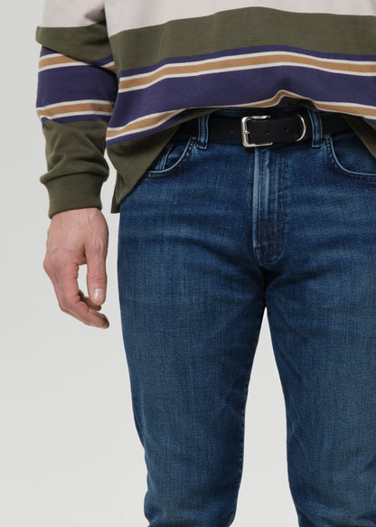 Person wearing a striped long-sleeve shirt and blue jeans on a grey background