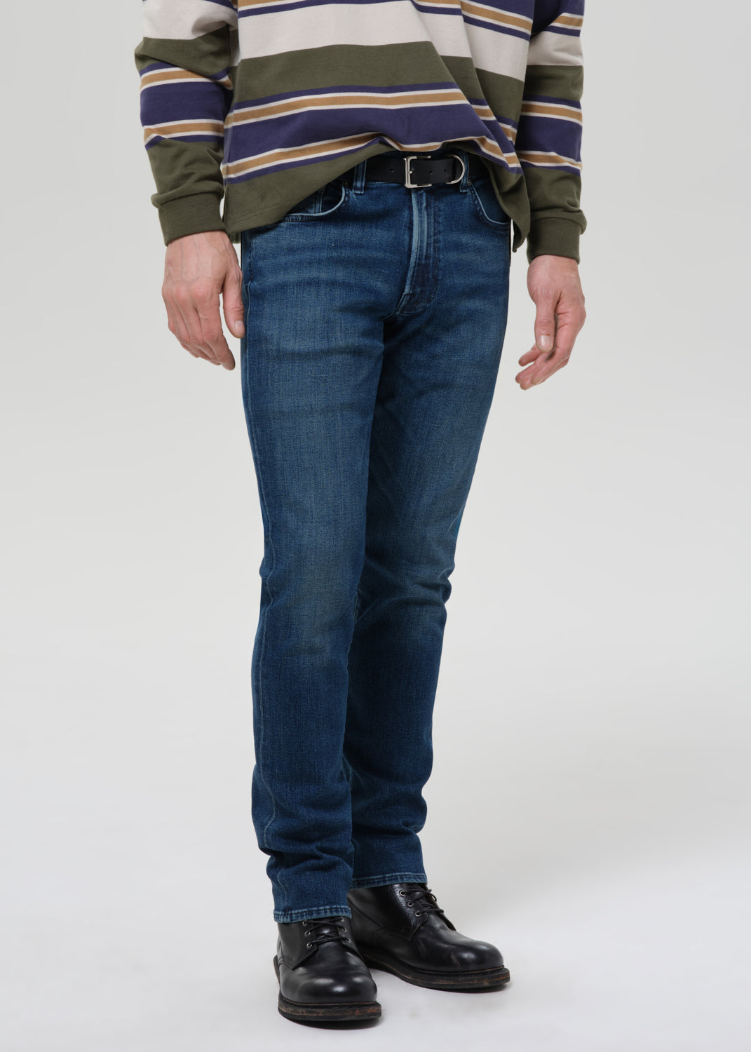 Person wearing a striped sweater, blue jeans, and black shoes on a grey background