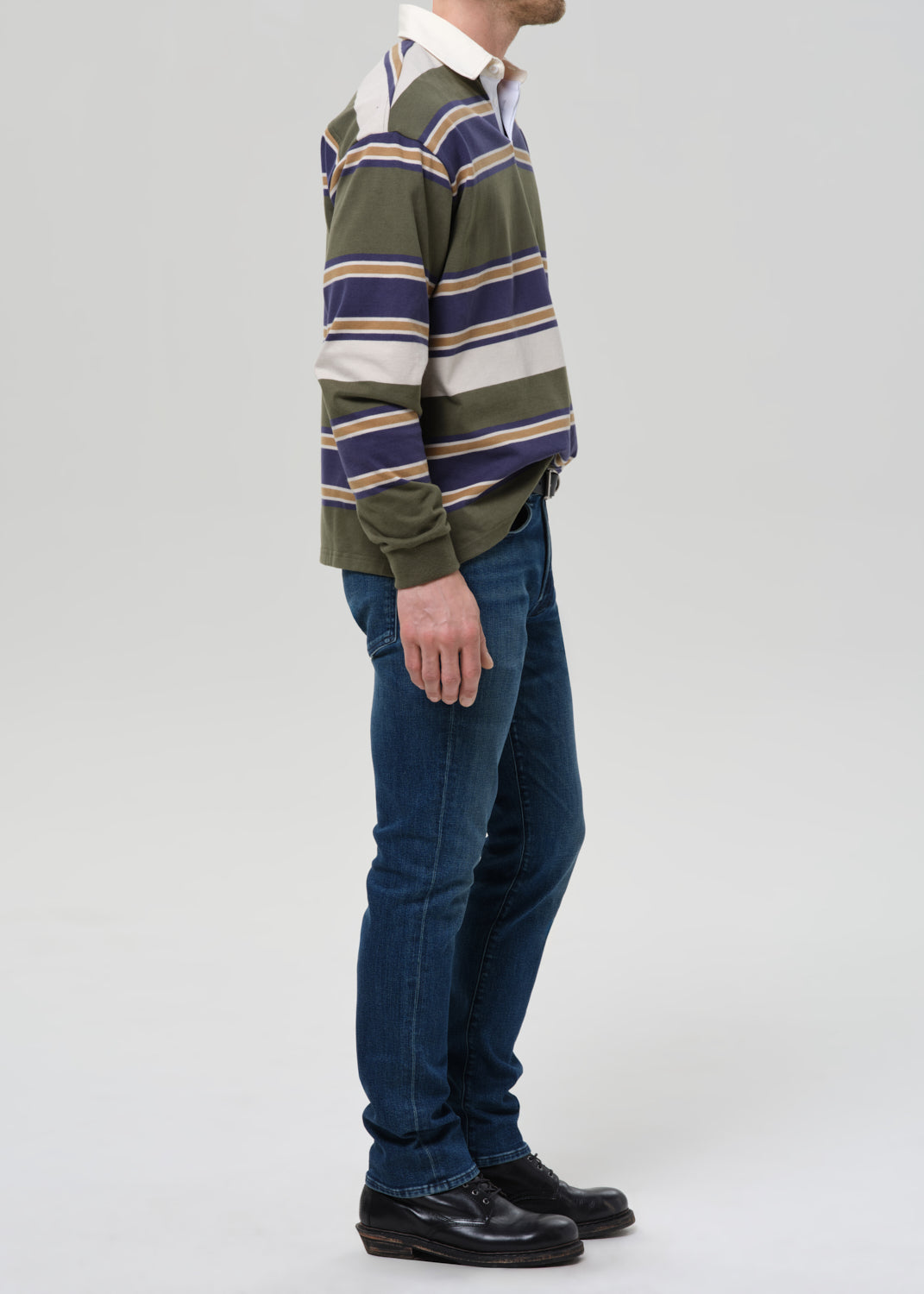 Person wearing a striped rugby shirt and blue jeans on a grey background