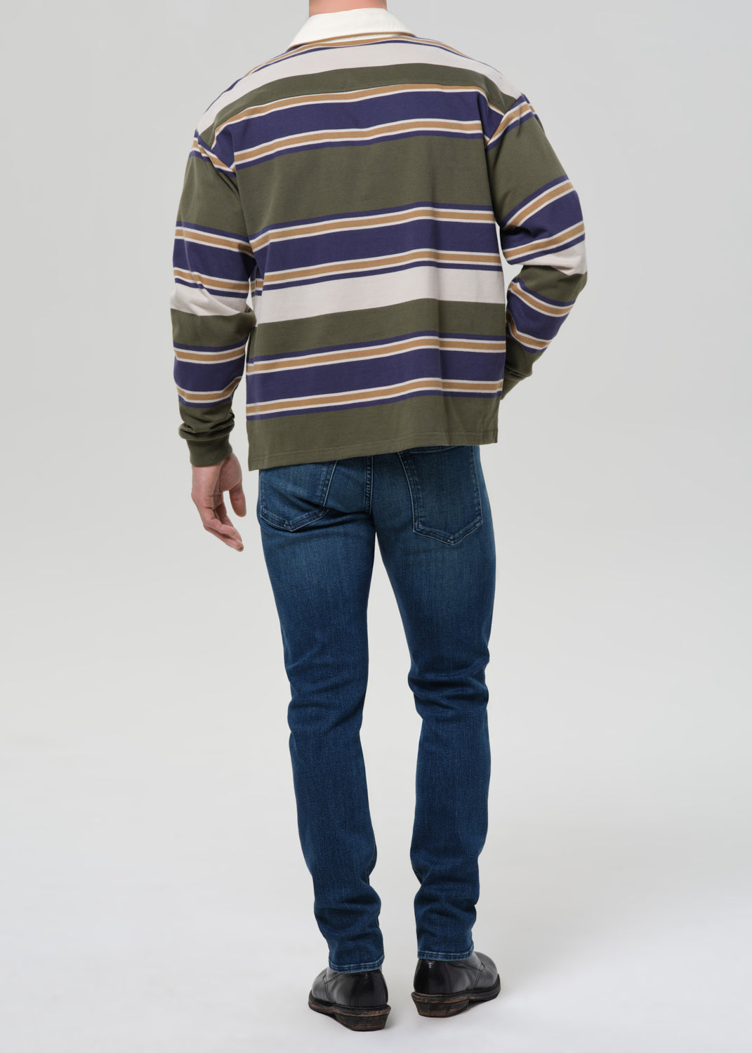 Person wearing a striped sweater and blue jeans on a grey background