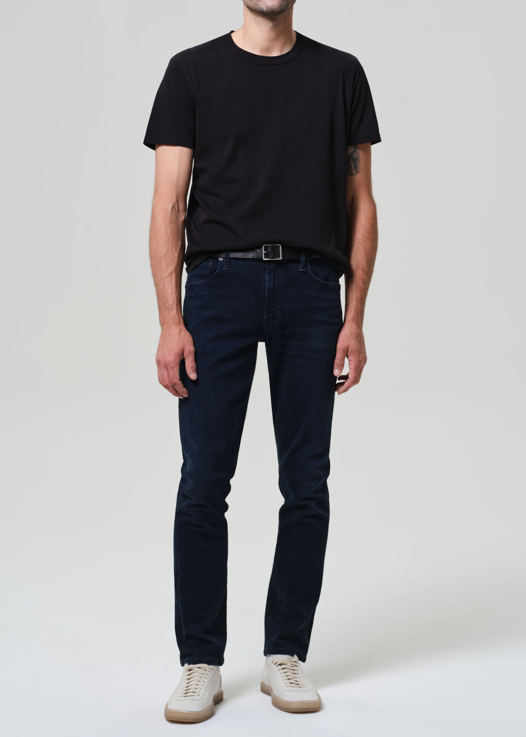 Person wearing a black t-shirt and dark blue jeans on a grey background