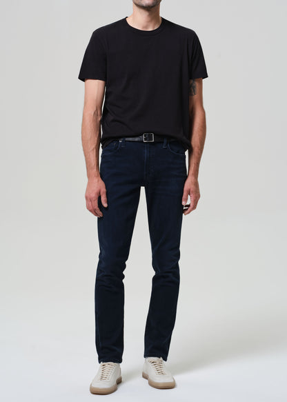 Person wearing a black t-shirt and dark blue jeans on a grey background