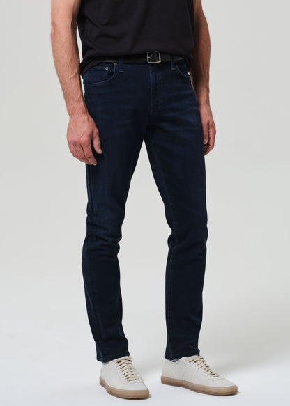 Person wearing a black t-shirt and dark blue jeans on a grey background