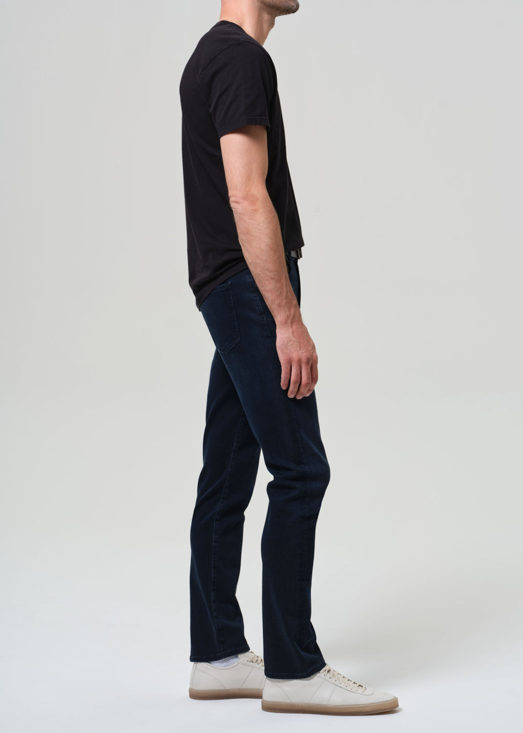 Person wearing a black t-shirt and dark blue jeans on a grey background
