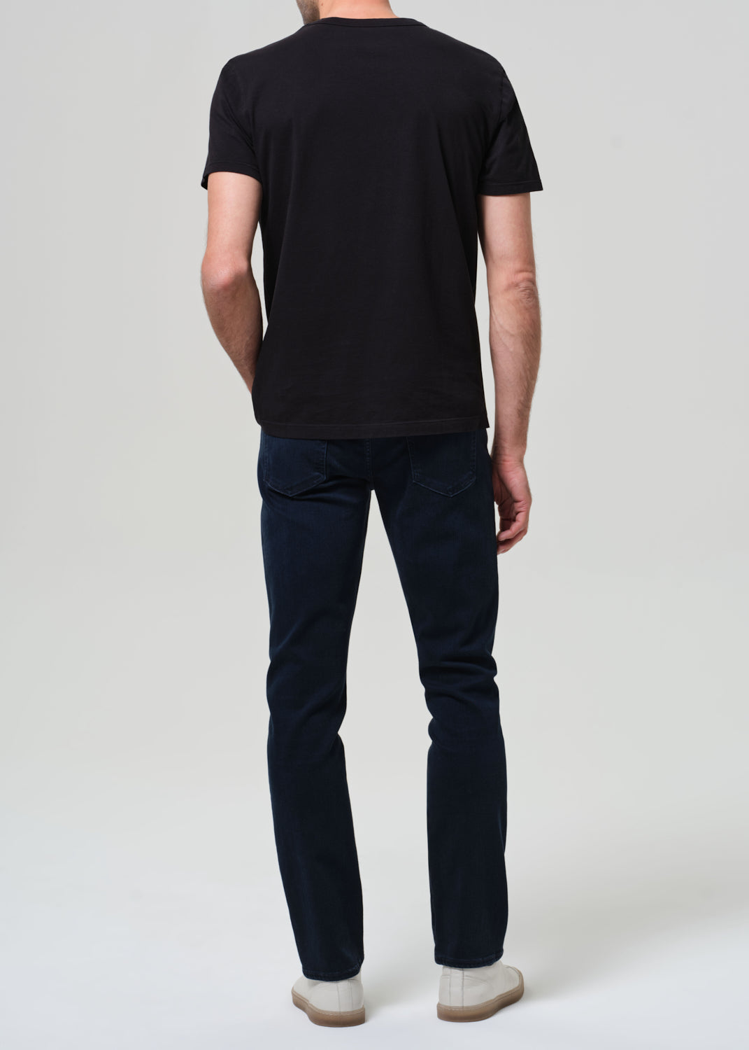 Person wearing a black t-shirt and dark blue jeans on a grey background