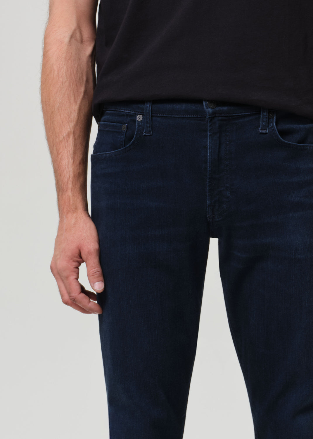 Person wearing a black t-shirt and dark blue jeans on a grey background