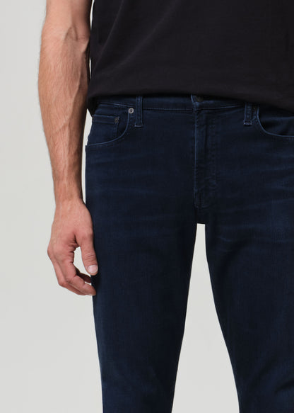 Person wearing a black t-shirt and dark blue jeans on a grey background