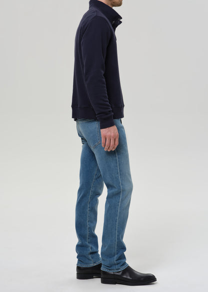 A man shown in profile wearing a dark navy quarter-zip fleece, light blue jeans, and black leather boots, standing against a grey background.