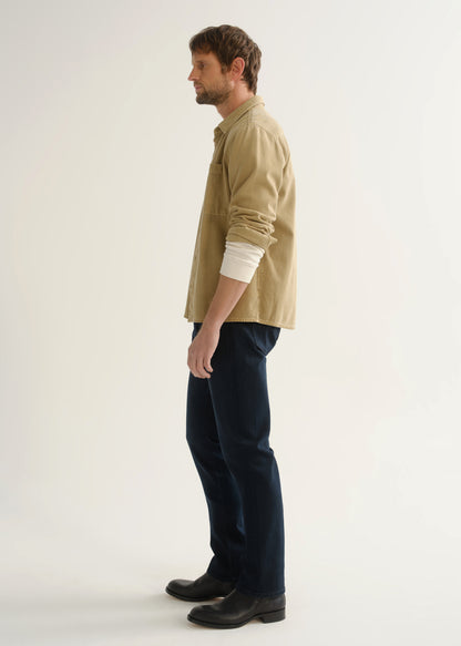 Person wearing tan button-down shirt and dark indigo jeans side