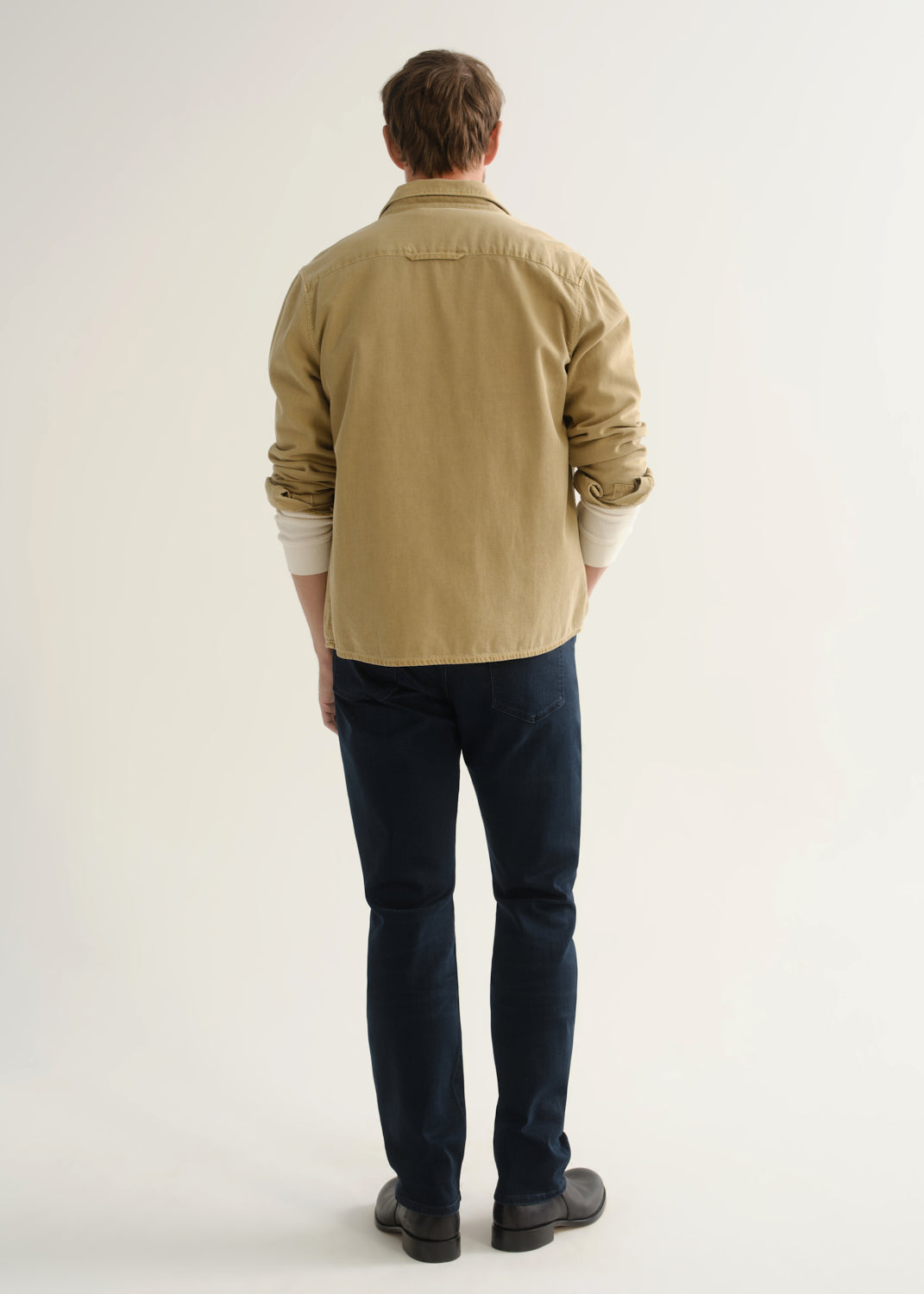 Person wearing tan button-down shirt and dark indigo jeans back