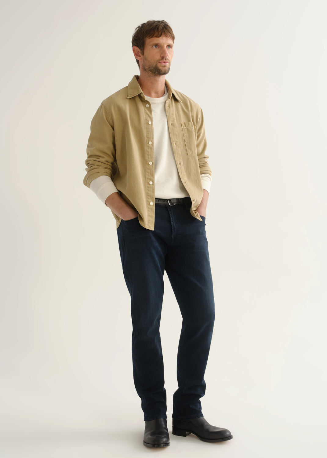 Person wearing tan button-down shirt and dark indigo jeans front three-quarter view