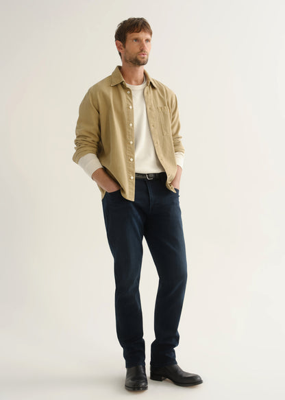 Person wearing tan button-down shirt and dark indigo jeans front three-quarter view